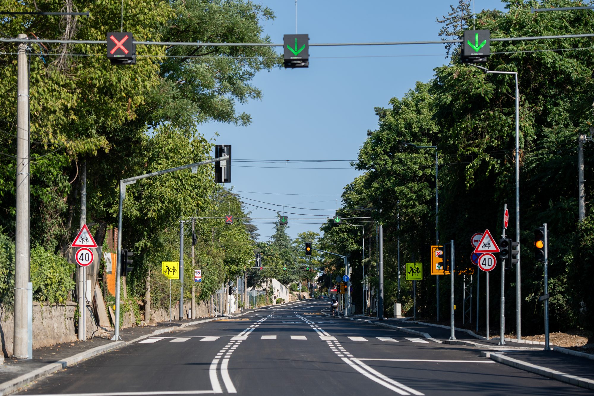 Overhead lane signals with a red cross and green downward arrows above a city street